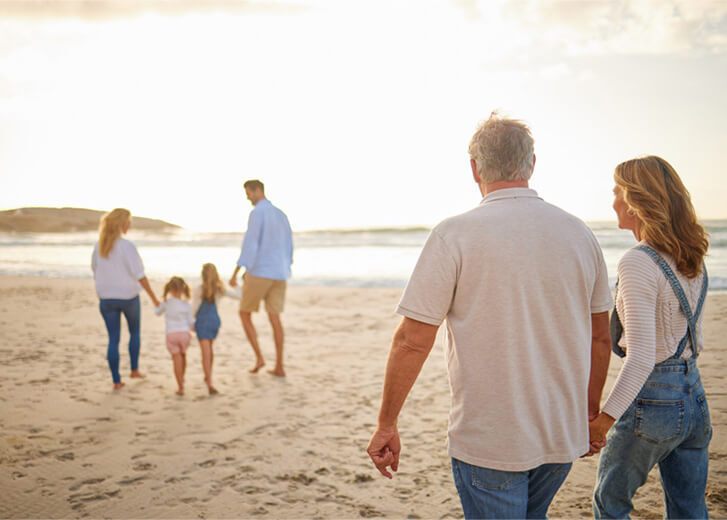 Rear view of Multi generation family holding hands and walking along the beach together. Caucasian family with two children, two parents and grandparents enjoying summer vacation